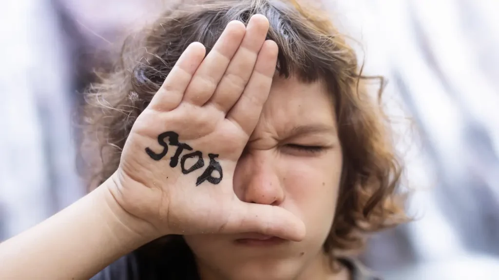 Fotografia de uma jovem com a mão a frente do rosto, na mão está escrito "Stop"