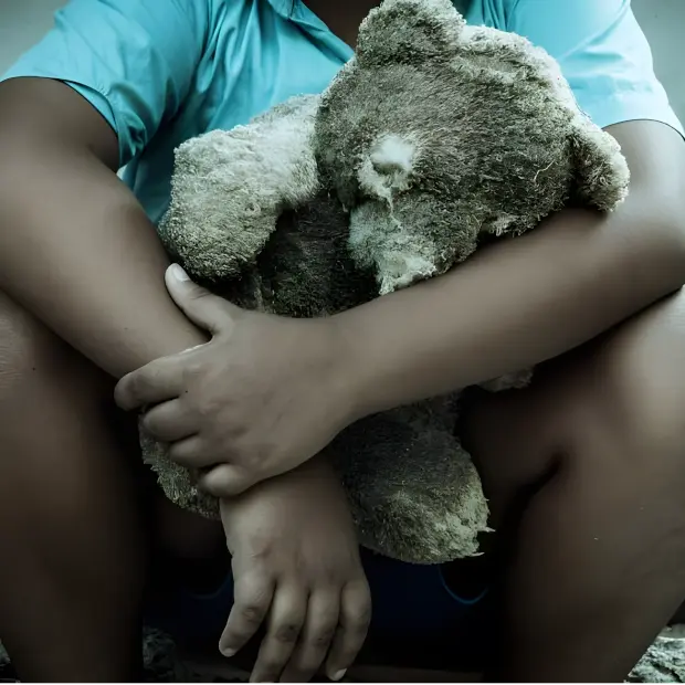 Fotografia de uma criança em um ambiente pesado segurando um ursinho ragado