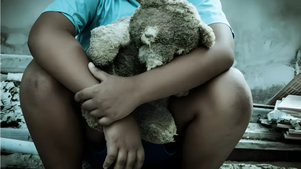 Fotografia de uma criança em um ambiente pesado segurando um ursinho ragado